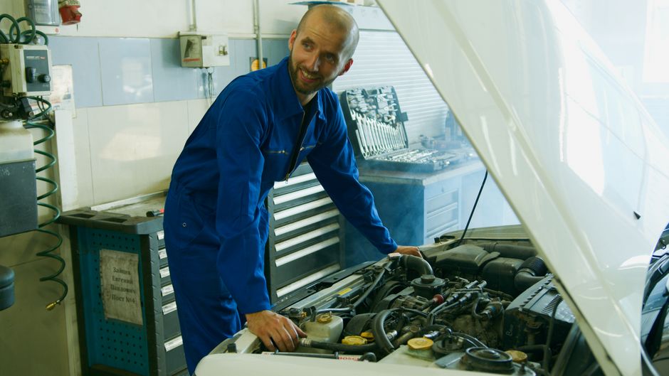 A smiling mechanic inspecting a car engine in the Ironwood Auto Repair garage